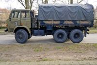 Trzyosiowa wojskowa ciężar&oacute;wka transportowa w barwach ochronnych (kamuflażu) z plandeką, stojąca profilem bocznym na drodze